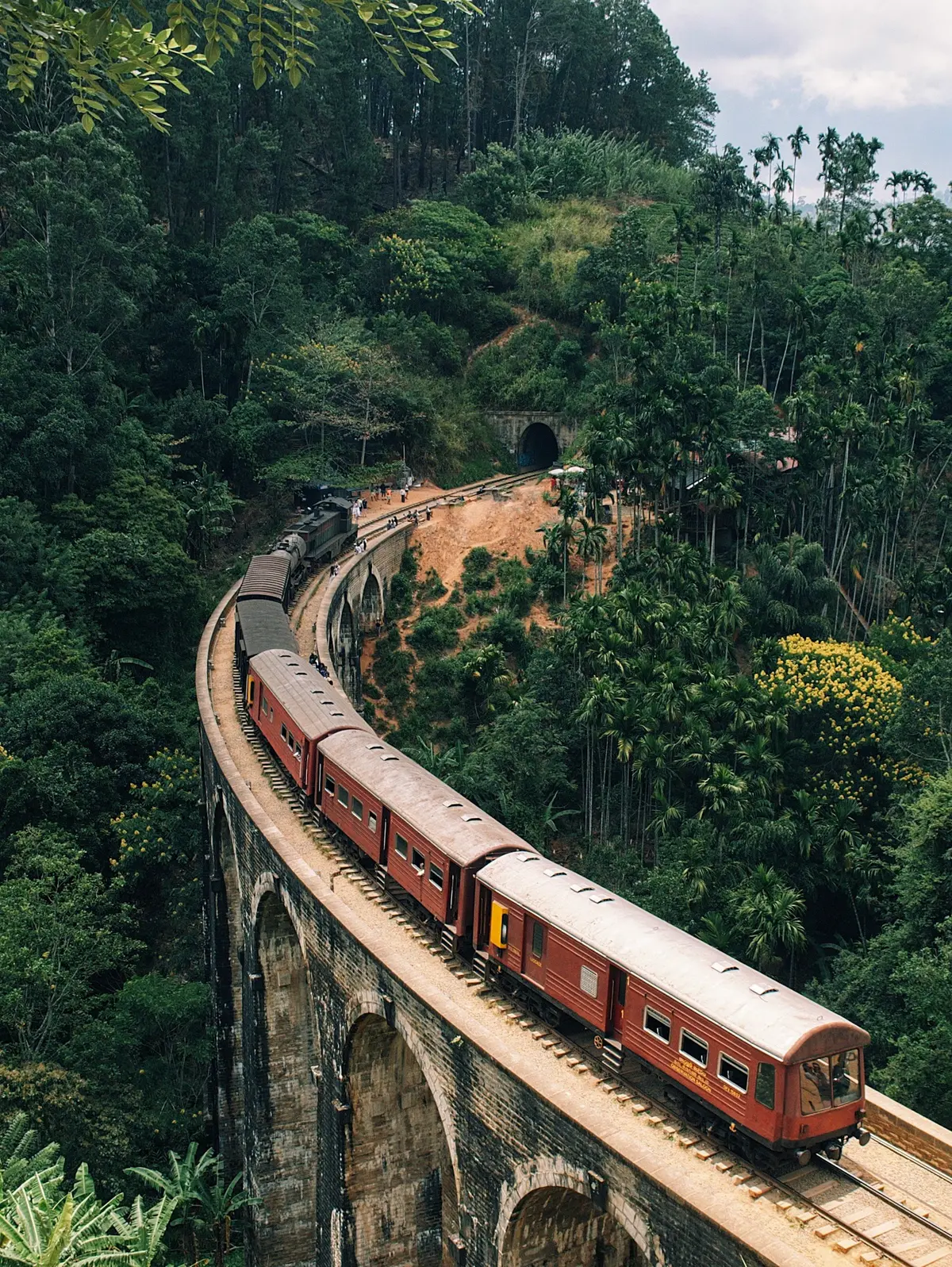A red train crossing the Nine Arch Bridge surrounded by green jungle in Ella